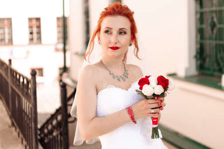 Portrait of a young beautiful bride in red sneakers with bouquet of roses on the city streetの写真素材