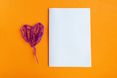 Purple thread handmade heart and white mockup blank on bright orange background, copy space for the...