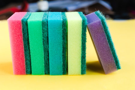 Stack of multicolor sponges for washing dishes on bright yellow background, close up, side viewの写真素材