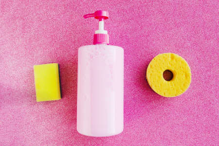 Bottle with pink dishwashing liquid and sponges for washing on pink glitter background. minimal concept. copy spaceの写真素材