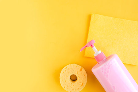 Bottle with pink dishwashing liquid and sponges on bright yellow background. minimal concept. copy...