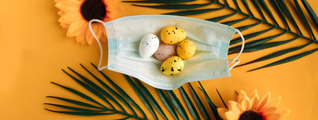 Quail eggs in face medical mask and palm branches on yellow background. Easter holiday during the...