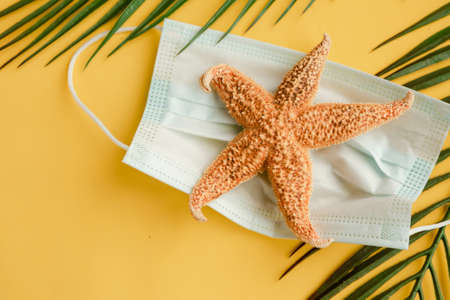 Starfish and face medical mask on bright yellow background. Coronavirus travel conceptの写真素材