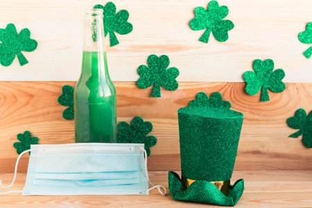 Green beer bottle, leprechaun and face medical mask on wooden background. Corona Patrick's Day...