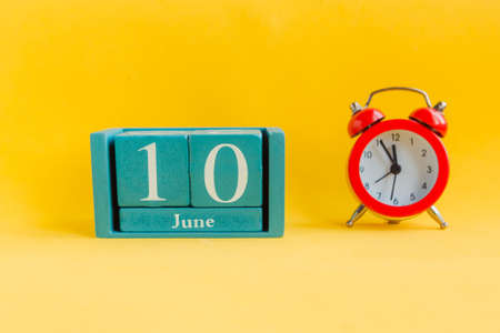 June 10. Blue cube calendar with month date and alarm clock on bright yellow backgroundの写真素材