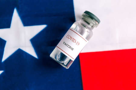 COVID-19 vaccine bottle on American flag background. Coronavirus in America conceptの写真素材