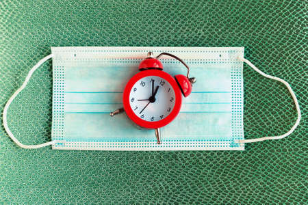 Face medical mask and alarm clock on color pattern background. minimal conceptの写真素材