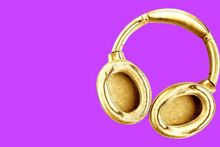 Big modern golden headphones isolated on bright purple background. Minimal concept. Copy space for the textの写真素材