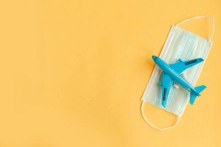 Toy airplane and face medical mask on yellow background. Travel during the pandemic concept. Copy spaceの写真素材