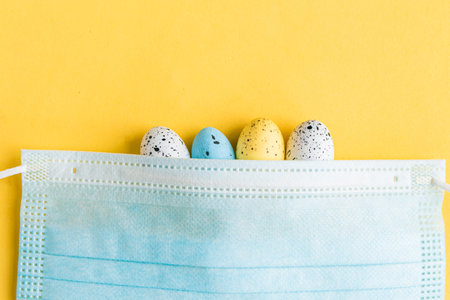 Quail eggs and face medical mask on bright yellow background. Easter concept