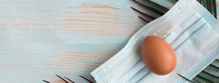 Chicken egg in face medical mask and palm branch. Easter holiday during the pandemic. Copy space