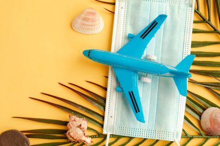 Toy airplane and face medical mask on yellow background. Travel during the pandemic concept