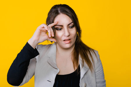 Portrait of young brunette thoughtful woman in studio with yellow isolated background.