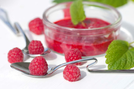 Mashed raspberries in a glass, raspberry on spoon, lemon balm