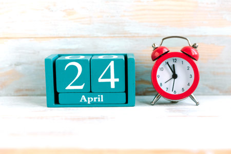 April 24. Blue cube calendar with month and date and red alarm clock on wooden backgroundの写真素材
