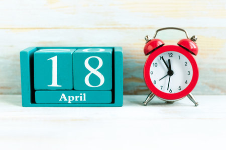 April 18. Blue cube calendar with month and date and red alarm clock on wooden backgroundの写真素材