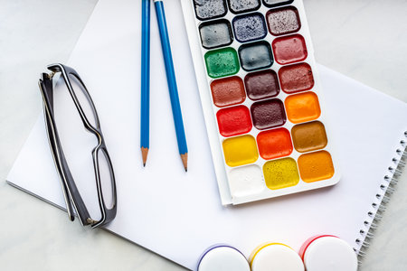 Watercolor paints, pencils and glasses on a white background.の写真素材