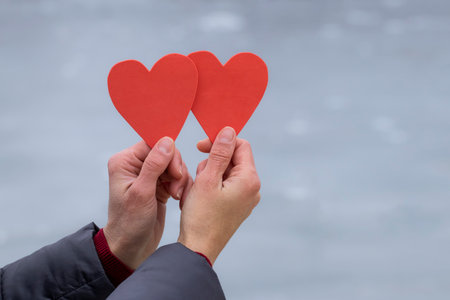 Women's frozen hands in winter.Female hands with dry red skin hold two paper hearts on a background of snow.Importance of skin care in winter.の写真素材