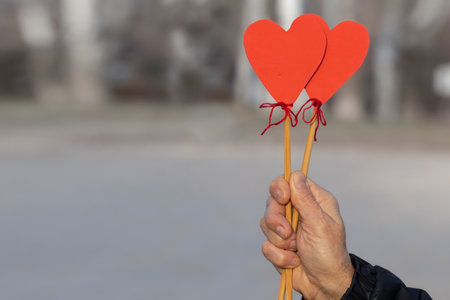 A hand holding two red heart shapes on sticks against a blurred background. Symbol of love and friendship.の写真素材