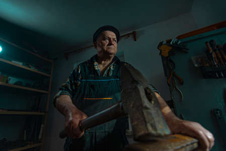 Elderly man with a hammer works in a workshopの写真素材