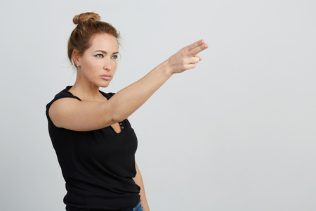 Emotional beautiful young adult woman portrait. Studio shoot. Isolated on White Background. A woman looks to the right upward, screwing up eyes, raising hand and simulating a shot with two fingers.の写真素材