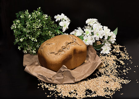 Loaf of homemade rye bread on a background of scattered grains, black background, horizontally, side viewの写真素材