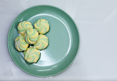 Colorful fluffy marshmallows on a green dish on a glossy white background, close-up, flat lay, top view, horizontal, copyspaceの写真素材