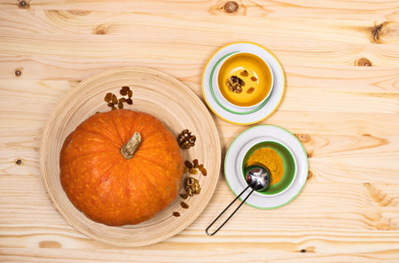 Yellow-orange pumpkin, raisins and walnuts lie on a wooden dish on a light wooden surface in a circle of colored tea utensils, top view, copyspaceの写真素材
