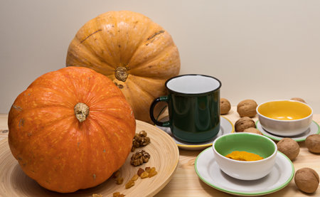 Yellow-orange pumpkin, raisins and walnuts lie on a wooden dish on a light wooden surface in a circle of colored tea utensils, horizontal, side viewの写真素材