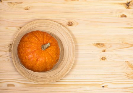 Yellow-orange pumpkin lies on a wooden dish on a light wooden surface, top view, copyspace on the rightの写真素材