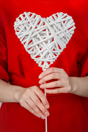 A woman in a red dress holds a white wicker heart in her hands, vertically, copyspace, closeupの写真素材