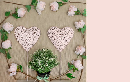 Decorative braided hearts on a natural background surrounded by delicate roses and a green plant, close-up, top view, white and green on beigeの写真素材