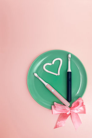 Composition with a heart made of toothpaste and two electric toothbrushes on the background of a green dish with a bow, top viewの写真素材