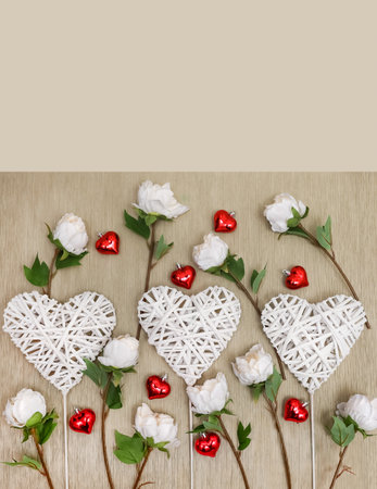 Decorative braided hearts on a natural background surrounded by delicate roses and small shiny hearts, close-up, top view, white, red and green on a beige backgroundの写真素材