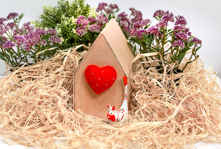 Buying a house, apartment, mortgage; plywood house with a soft heart with a walking toy kitten on a background of straw and purple flowers of clover, horizontal, close upの写真素材