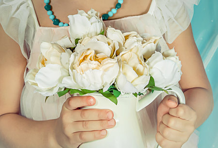 A girl in a light dress holding a bouquet of white flowers in a jug close-upの写真素材