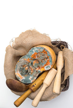 Orange moldy cut of a pumpkin surrounded by kitchen utensils on sackclothon a white background, mold and mildew on food, mold development, frequent problems, texture, top view, copy spase, verticalの写真素材