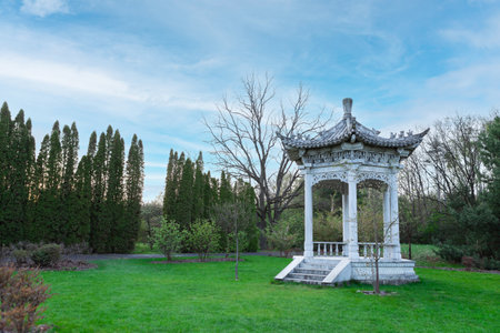 A white marble Chinese garden pavilion with intricate carvings and surrounded by trees in a park. Open, airy, and octagonal design with latticework on walls and roof.の写真素材