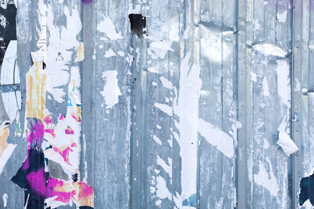 The tattered remains of fly posters on a weathered urban wall create an abstract and captivating...