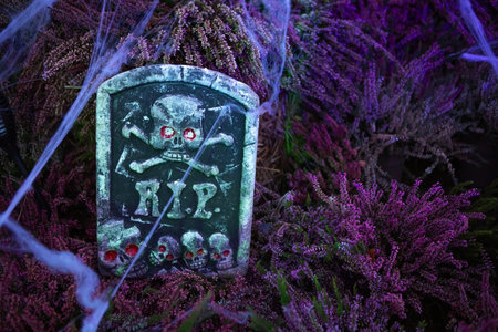 A tombstone-shaped Halloween decoration with a skull and crossbones design. The tombstone is made of plastic and has red glowing eyes. It is perfect for decorating your yard or garden for Halloween.の写真素材