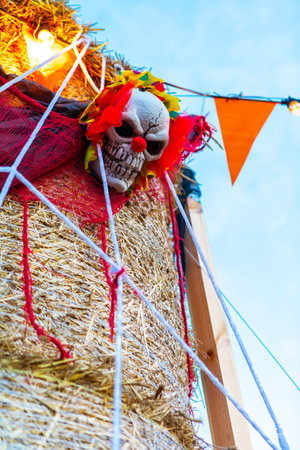 This is an image of a Halloween haybale with a skull on top of it. The haybale is isolated on a blue sky background. It can be used for Halloween-themed projects or as a background for text.の写真素材
