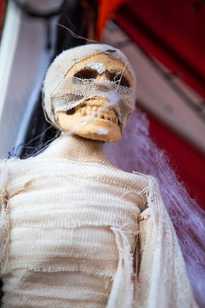 A spooky mummy in white gauze, great for Halloween. This eerie picture shows a mummy with a skull head, wrapped in torn gauze, on a red backdrop. Perfect for horror-themed projects.の写真素材