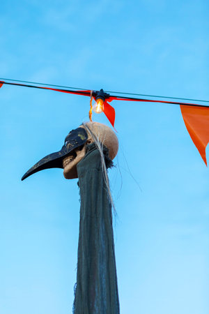 Halloween skull decoration with flickering lightbulb, orange flags, and a skull in a black plague doctor mask, creating a spooky and mysterious atmosphere for celebrations.の写真素材