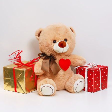 A charming teddy bear with a red heart on its chest sits between two beautifully wrapped gifts. Ideal for Valentines Day, birthdays, or special occasions, this gift conveys love and warmth.の写真素材