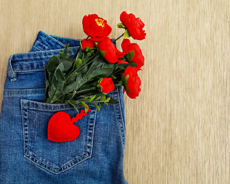 A stunning bouquet of bright red flowers in full bloom rests in the back pocket of dark blue jeans. The colorful image exudes vibrancy and style, creating a unique fashion statement.の写真素材