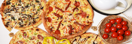 Different types of pizza on a round white table surrounded by tea utensils and cherry tomatoes, flat lay, close-up, horizontalの写真素材