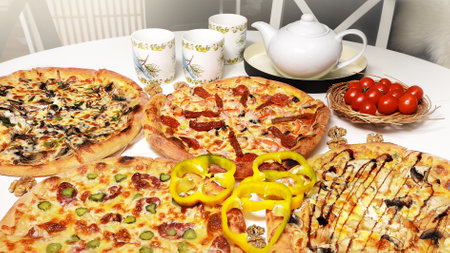 varied pizza on a round white table surrounded by tea utensils and cherry tomatoes, close-up, bannerの写真素材