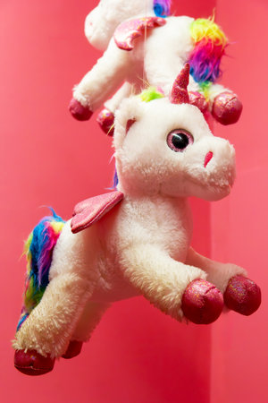 Whimsical unicorn plush toys dangle cheerfully from above, their vibrant rainbow manes and sparkling accents catching the eye. The bright pink background enhances their playful charm, inviting joy.の写真素材