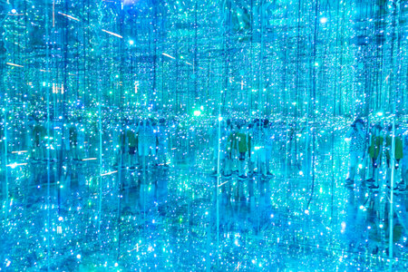 Groups of visitors explore a captivating art installation illuminated by countless blue lights and mirrors, creating a mesmerizing atmosphere. The experience invites deep engagement and reflection.の写真素材