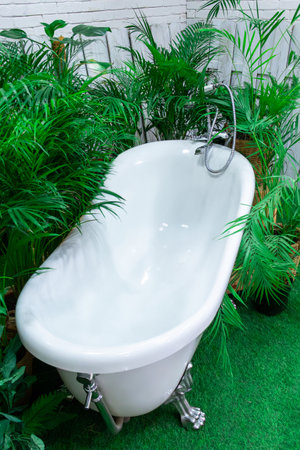 A luxurious freestanding bathtub is nestled among vibrant green plants in a serene garden. Sunlight gently filters through foliage, creating a calming atmosphere perfect for relaxation.の写真素材